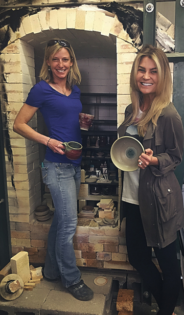 Julie Anderson (left) and student Kayt Gary (right) unload the reduction kiln during a kiln opening party at Warehome Studios, 2017. Photo by Megan Westercamp.