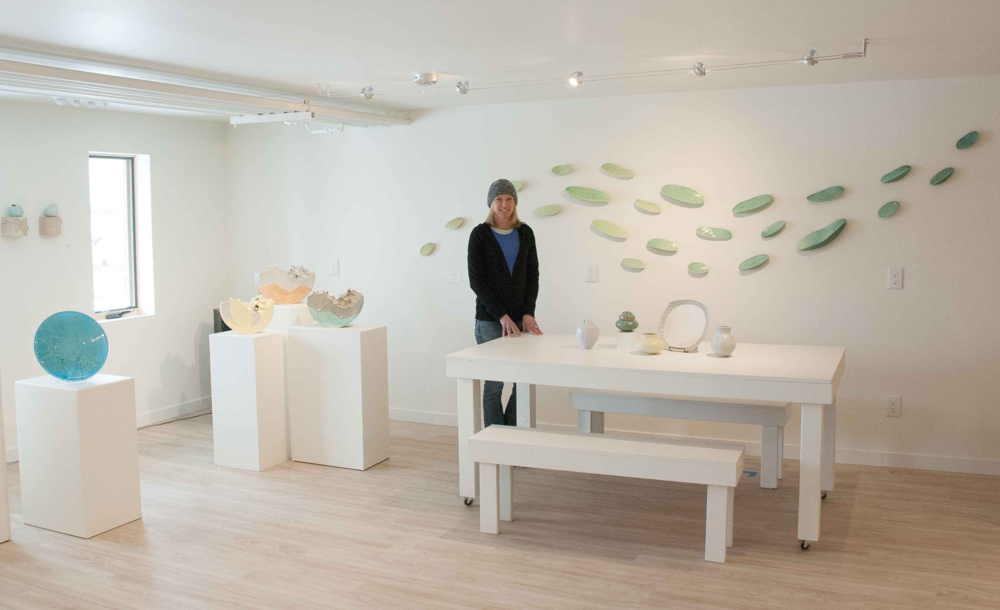 Julie K. Anderson in the Warehome Studios Gallery.  Glass plate on left by Gregory Grasso, all other work by Anderson; large wall sculpture behind Anderson titled “Ripple,” 2016. Photo by Megan Westercamp.