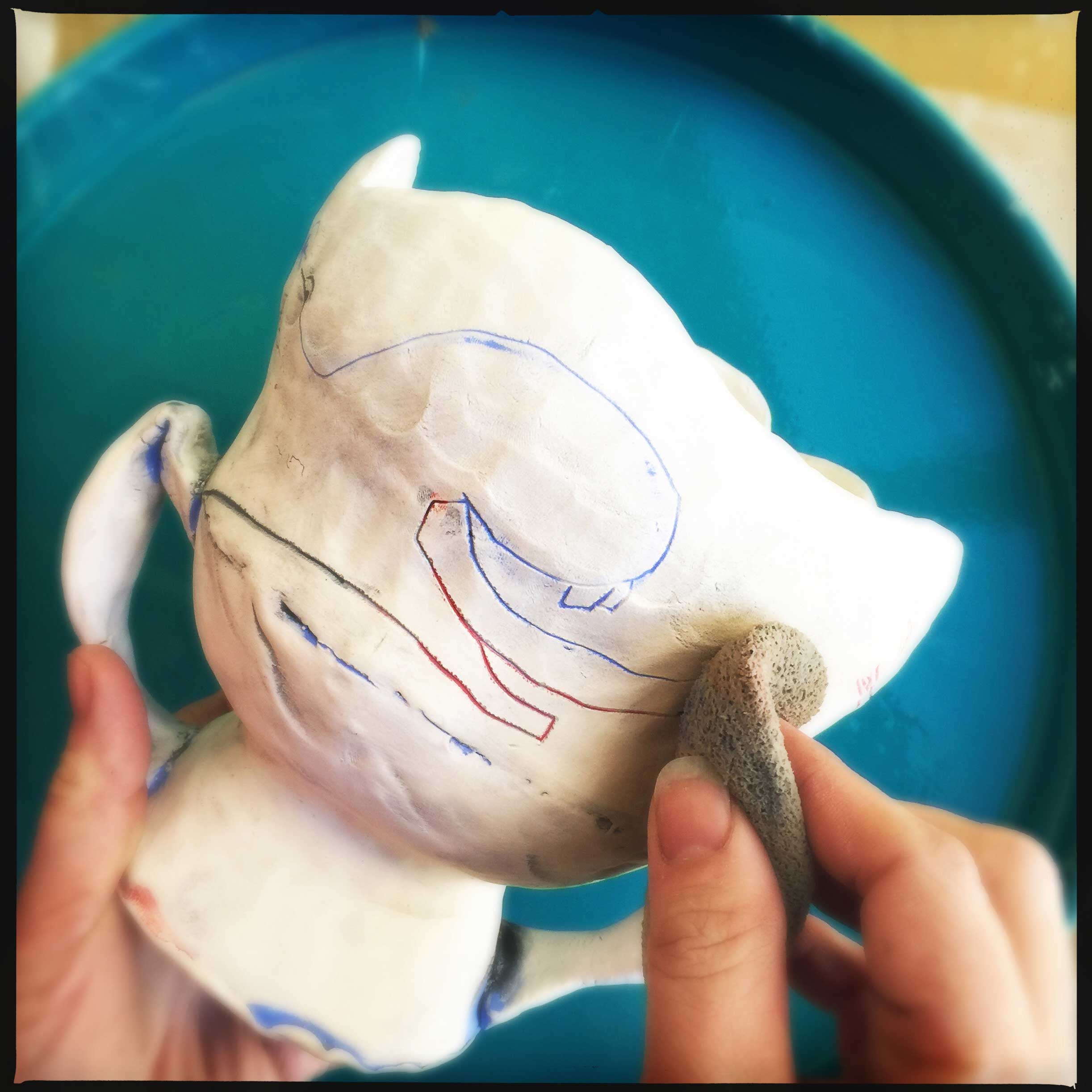 Cambric applies her underglaze to a bisque piece and wipes off the excess. Photo by artist, 2015.