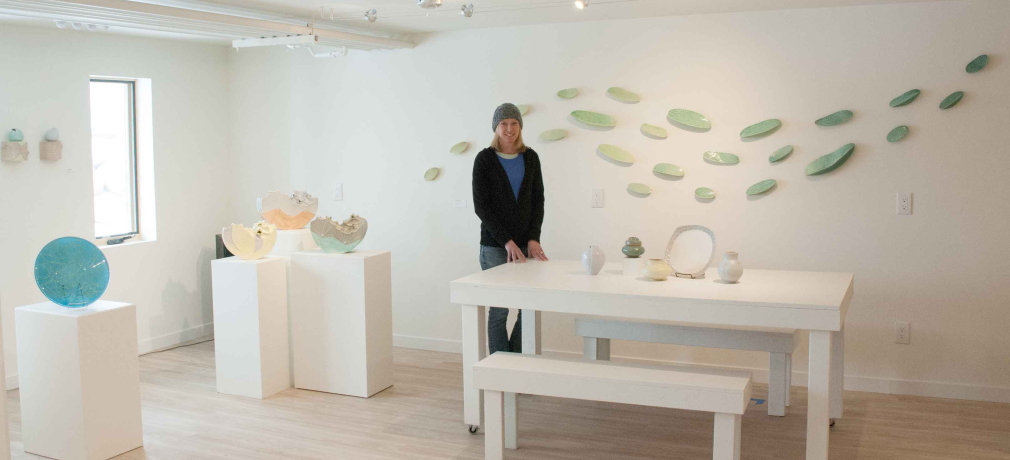 Julie K. Anderson in the Warehome Studios Gallery.  Glass plate on left by Gregory Grasso, all other work by Anderson; large wall sculpture behind Anderson titled “Ripple,” 2016. Photo by Megan Westercamp.