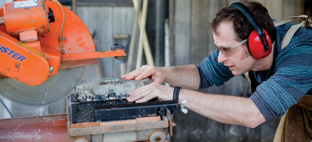 Mess slices a fired sculpture from his Reclaim series on a diamond wet saw outside his home studio. Photograph by Erin Little, May 2015.