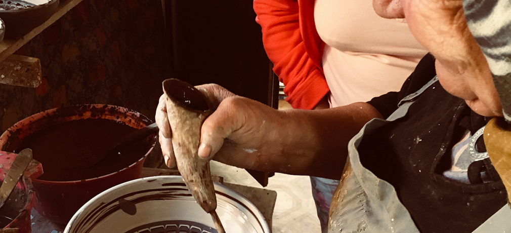 Olari women decorates a bowl in a slip-trailing technique using a hollow bull’s horn and a feather quill.