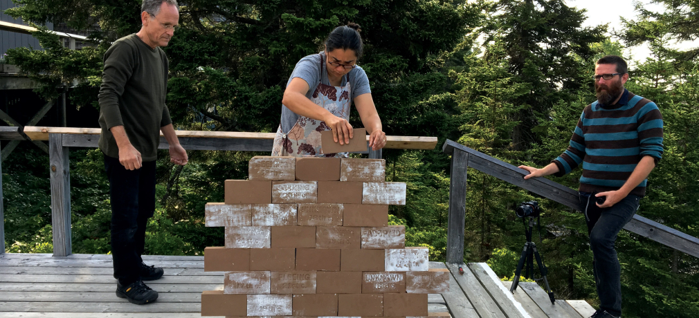 L to R: Jack Wax, Ayumi Horie, and Elliott Clapp stack workshop participants' bricks stamped with words such as fleeing, seeking, here, stolen, and adopted, that describe their immigrant stories or identities. Photo courtesy of Horie.