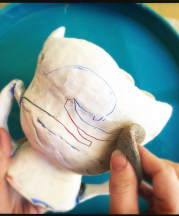 Cambric applies her underglaze to a bisque piece and wipes off the excess. Photo by artist, 2015.