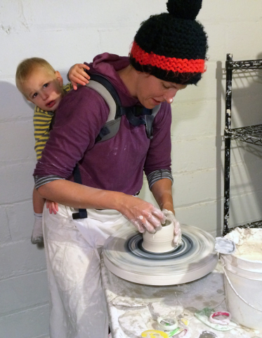 Kate Fisher with her son in her studio, at the potter's wheel. 